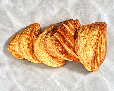 A row of glazed turnovers with leaf scoring, on baking parchment.